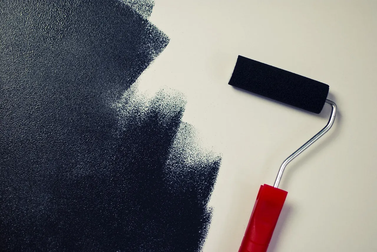 Paint roller applying a dark coat to a white wall