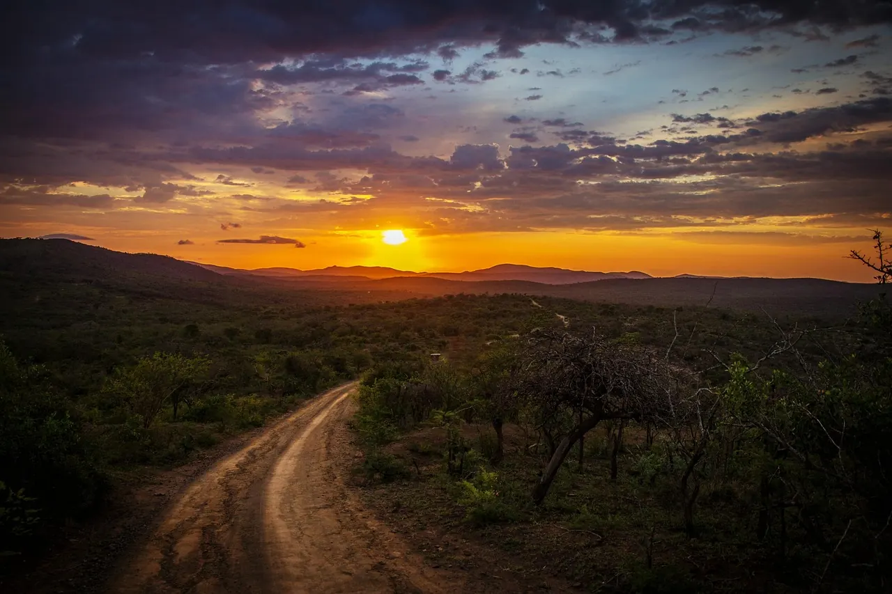 Rural murram road winding through hills at sunset