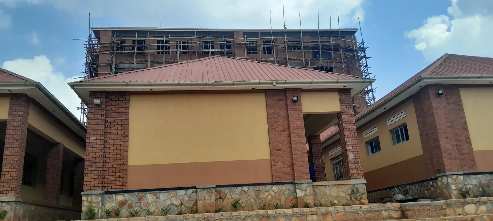 Multi-storey school block under construction behind completed classrooms